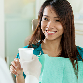 A dental patient smiling and taking a cup of water